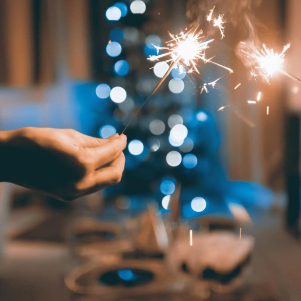 Hands holding sparklers in a festive indoor setting with blurred lights and bokeh effect.