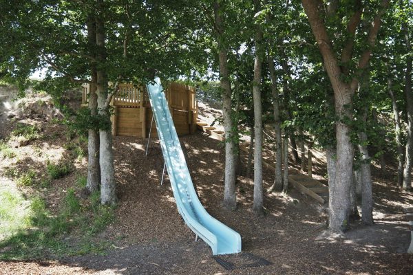 A blue slide in a wooded playground area with trees.
